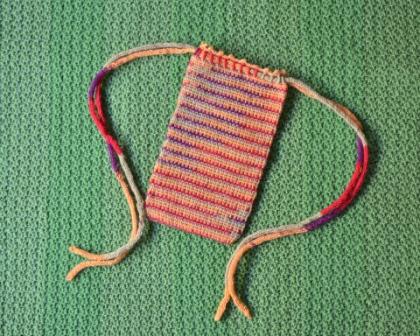 Striped bag laying flat on a crocheted green backdrop. The straps have been arranged so their ends touch the bottom corners of the bag.