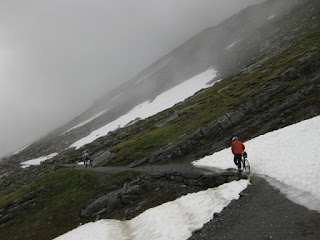 Cyclists traversing the gravel path next to snowbanks, Gemmipass, Switzerland