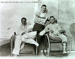 Black and white photo of three men with disabilities, two in wheelchairs two missing arms,