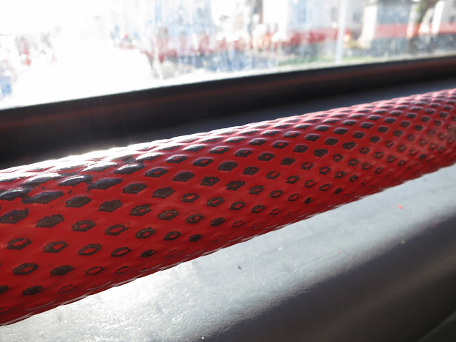 Red hand rail with dark, diamond grip at front of top of double-decker bus.