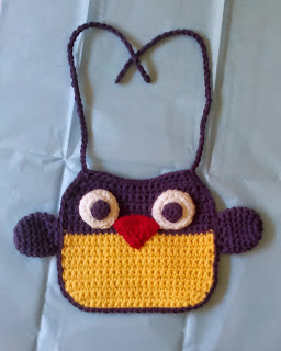 Owl Bib: the bottom half (owl body) is yellow and the top half (owl head) is purple. The bib has a purple border and purple ties.  Purple wings are attached to the side.  The appliquéd eyes are big round circles with smaller purple circles inside. The appliquéd beak is a red triangle. 