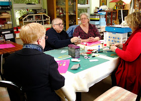 Group of four women around a workshop table, looking at bits of a miniature picnic basket kit.