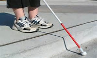Photo of a child's feet in sneakers standing on a one-step platform with a while cane for the blind out in front
