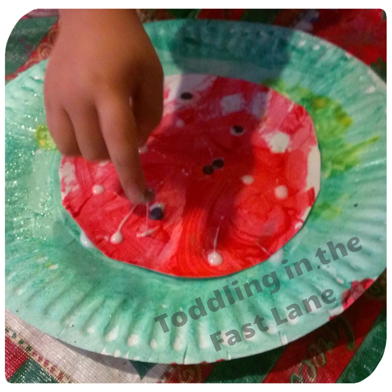 Paper plate crafts - child painting with finger on a paper plate watermelon craft