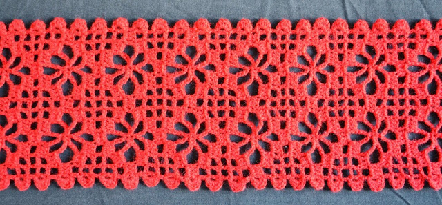 Close-up of a red spider stitch scarf that I completed in January 2015.  The large holes are part of the spider stitch design. The smaller holes are part of a filet grid.  The border pattern uses bumpy shapes..