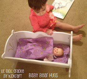 toddler with Kidkraft Lil' doll cradle and madame alexander doll reading a book