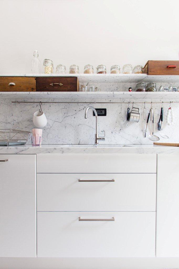 Kitchen with sleek white cabinetry and beautifully styled marble open shelving. Image via Cote Maison