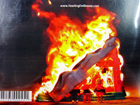 Back of a CD, showing a picture of a burning Fisher Price dollhouse.