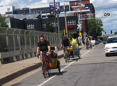 A series of bicycles pulling trailers with the contents of a house on them, including mattresses