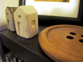 Two tiny pottery houses on display next to a giant wooden button.