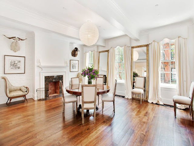 grand dining room with wood floors, a marble fireplace, a small round wooden table and two large decorative mirrors.