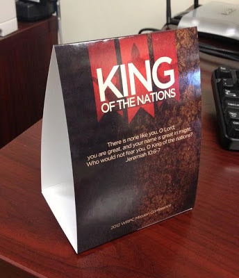 dark-colored promotional table tent on a table, featuring "King of the Nations", printed by GotPrint.com