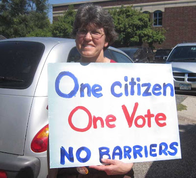 Woman holding hand-painted sign reading One Citizen One Vote No Barriers