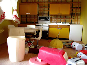 Messy vintage Lundby dolls house kitchen with dusty furniture and items strewn across the floor.