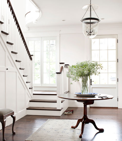 White foyer with wood floor, round table, Persian rug, and glass pendant light