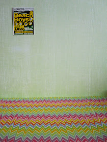 Bright 1960s Beach Boys poster on a green wall with a bright zig zag-patterned floor.