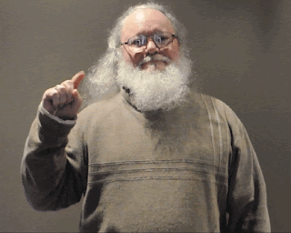 Animated GIF/cinemagraph of Jim Campbell standing still just waving one forefinger quickly and a small amount.