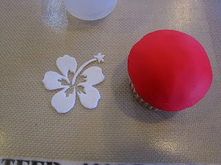 finished white fondant cut out of hibiscus nest to red fondant covered cupcake on baking mat 