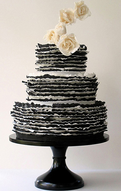 Set over three round tiers a black and white striped ruffle cake with cream Set over three round tiers a black and white striped ruffle cake with cream
