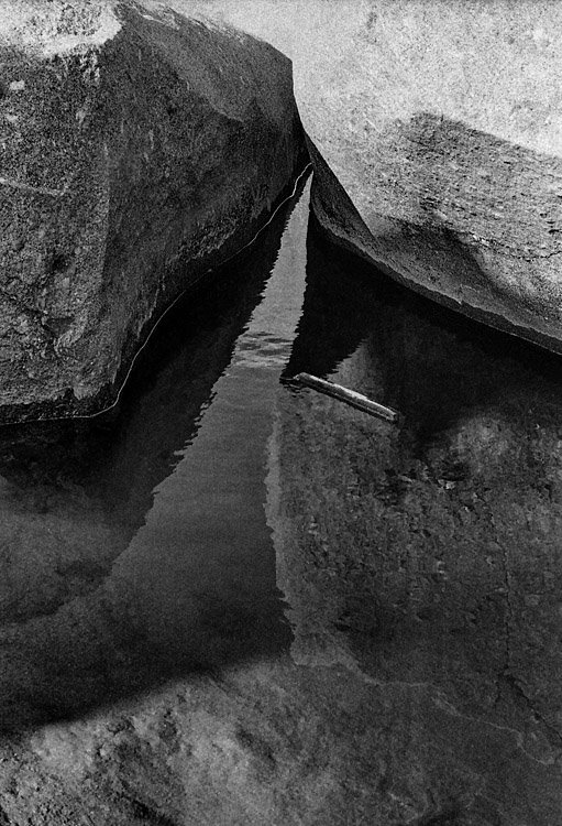 Pedra no charco Pormenor de um reflexo de duas rochas nas águas de um pequeno lago de água junto à praia