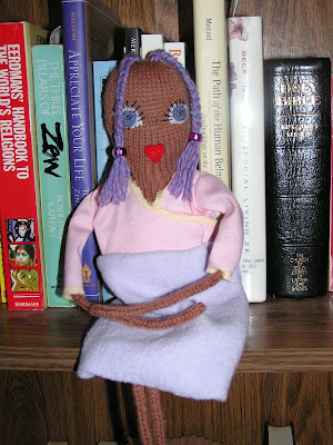 doll sitting on bookshelf in pink and lavender dress
