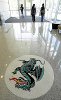 Entry way to a well lit lobby has a round white circle on the floor with a green dragon breathing fire in the white circle on the glossy lobby floor.