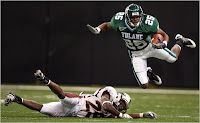 Leaping Tulane football player ball carrier dives past a defender left on the ground during a football field.
