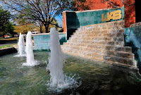 Gold UAB lettering on a green tile background that is part of a waterfall of stairs and vertically propelled water in the foreground.