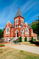 Brick church like Victorian style building atop a grassy knoll.