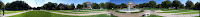 Panoramic view of a college campus with students walking under the sun across concrete walkways and grass. Brick academic buildings with white pillars are in the background at the SMU campus.