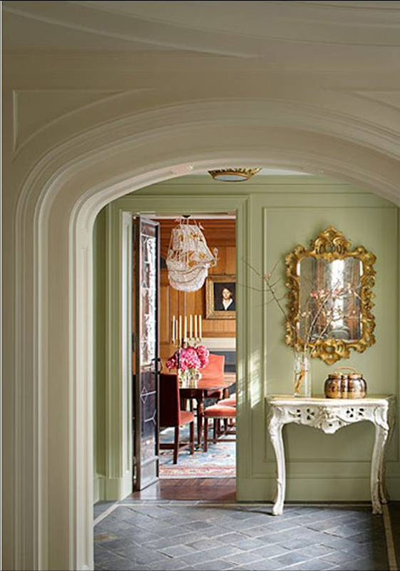 Room with pale green walls, a white console table with curved legs, an ornate gold mirror and stone tile floors outside a New York City apartment's dining room designed by Katie Leede