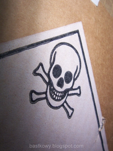 Częściowe zdjęcie kartonu z wyraźnie narysowanym symbolem czaszki i skrzyżowanych kości, używanym jako ostrzeżenie przed niebezpieczeństwem.