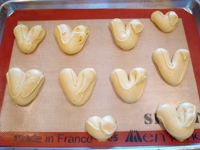 uncooked cream puff dough piped in a heart shape on a silpat liner