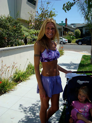 Woman in workout clothes standing next to young girl in stroller smiling