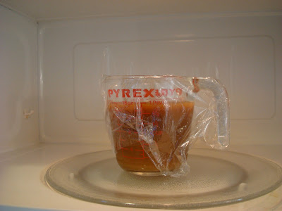 Gravy in measuring cup with plastic wrap in microwave