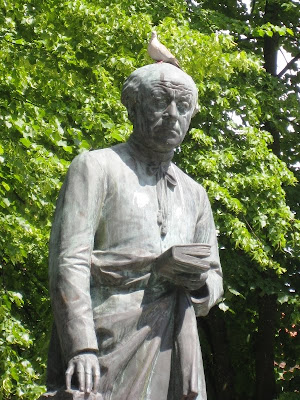 Bird perched on the head of a statue of a man holding a book
