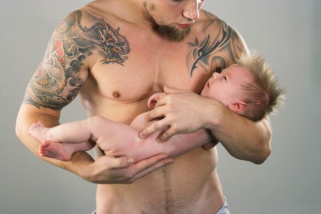 Shirtless man holding his baby has dragon tattoo from his arm to chest.