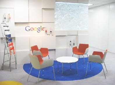 テーブルと椅子などがあって、壁にGoogle のロゴがある部屋を示す画像。