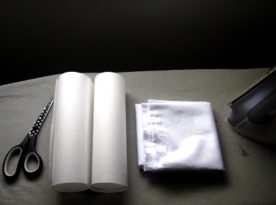 An ironing board with a pair of scissors, a rolled-up piece of paper, a piece of paper and an iron on it.