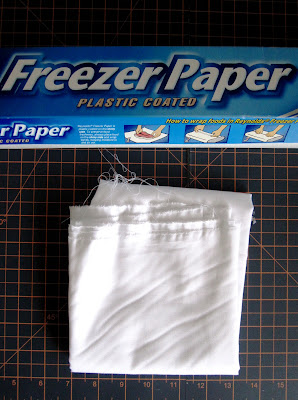 A roll of freezer paper and a length of white cloth on a cutting board.