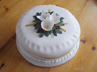 A round cake covered in white icing with flowers and holy on top