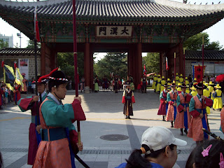 Men in colorful uniforms perorm teh changing of the guard at the palace gate with trumpets and drums