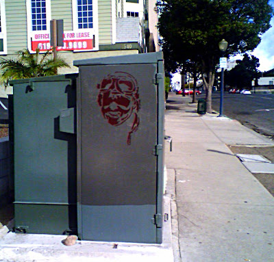 This is a green electric box with a maroon stenciled aviator face on it.