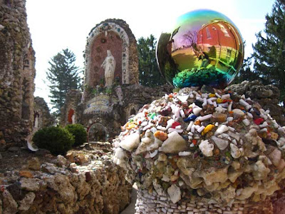 Irridescent gazing ball amid rock-covered structures with a statue of Jesus in the background