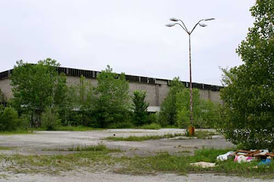 Ugly nondescript grayish mall building in disrepare with trees and weeds growing up all around it