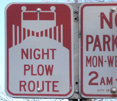Red and white street sign with iconic snow plow and a pile of snow, reading Night Plow Route
