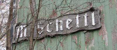 Green weathered barn wall with wooden sign reading M Schettl in blackletter style