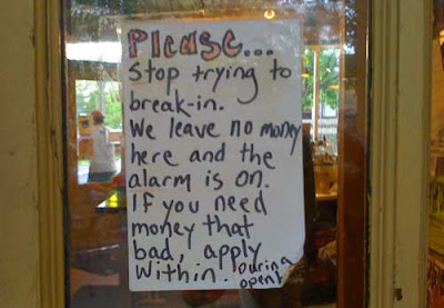 Handwritten sign in the window of a back door, reading Please stop trying to break in. We leave no money here and the alarm is on. If you need money that bad, apply within during open hours.