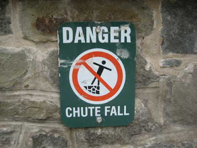 Sign that says DANGER chute fall with figure falling off a stone wall