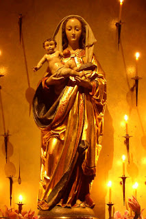 Child Jesus in the hands Mother Mary statue in golden lighting of bright Candles around free Christian religious image